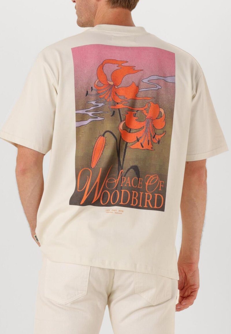 Beige t-shirt med kort ärm som har en stor blommig grafik i orange och rosa, med texten "Space of Woodbird" längst ner.