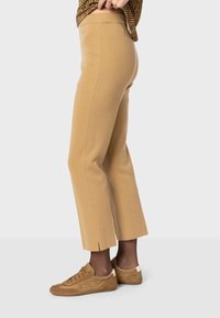 Pantalons beige cropped avec une texture lisse et une taille plate à l'avant, associés à des baskets en suède marron avec des accents blancs au talon.