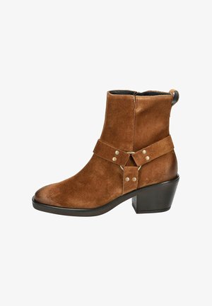 Bottine en cuir suédé marron avec une semelle rembourrée, un talon épais et un détail de large bandoulière ornée de clous en métal et d'un accent circulaire.