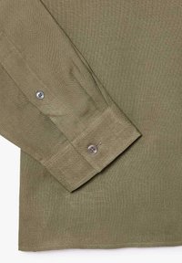 Polsino di camicia a maniche lunghe in tessuto verde oliva con cuciture visibili e due bottoni in plastica sul polsino e sulla patta della manica.