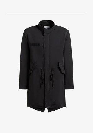 Crna duga parka jakna s visokim ovratnikom, prednjim džepovima s preklopom, vezicama u struku i malom oznakom marke blizu ruba.