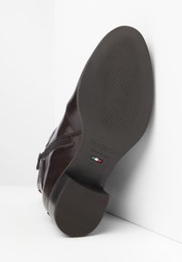 Stivaletto in pelle marrone con chiusura a zip, suola in gomma texturizzata e finitura senza giunzioni. Presenta un'impronta del logo e un dettaglio con la bandiera italiana sulla suola.