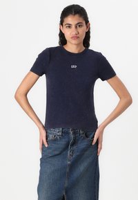Marineblå T-shirt i blødt bomuldsstof med ribbet tekstur og et lille hvidt "GAP" logo på brystet. Kortærmet, tætsiddende design.