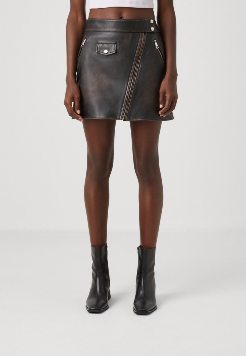 Svart läder minikjol med en sidokniv, framficka och tryckknapp. Slät textur med en något glänsande finish.