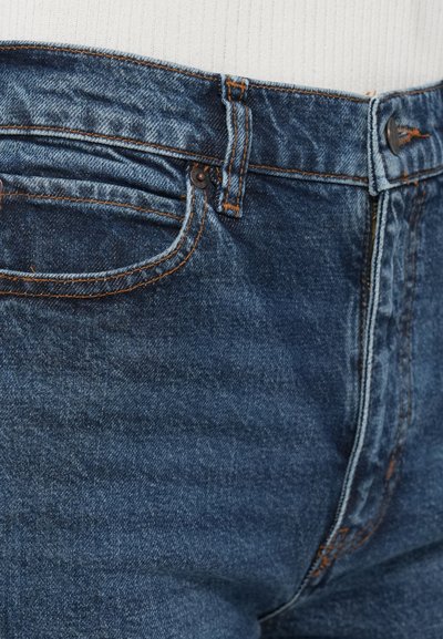 Tmavomodré džínsy z denimu s oranžovým prešitím, päťvreckovým dizajnom a zapínaním na gombíky vpredu. Hladká textúra a klasický strih.