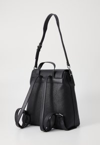 Sac à dos noir en matériau texturé, comprenant des sangles réglables, une poignée supérieure et un design structuré au look minimaliste.