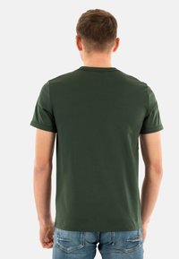 Camiseta verde de manga corta hecha de una tela suave. Presenta un escote redondo y una forma ajustada. Sin logotipos ni patrones visibles.