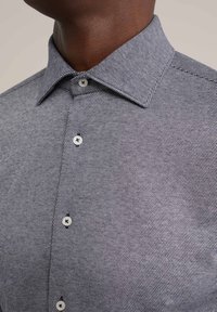 Camisa de manga corta con un patrón texturizado en blanco y negro, cuello de punta y cierre de botón con botones redondos de color claro.