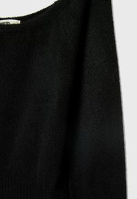 Pull noir en tricot avec une surface texturée et un large décolleté. Le tissu semble doux et légèrement duveteux. Ourlet côtelé en bas.