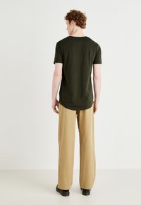Dark green cotton t-shirt, short sleeves, crew neck, paired with light beige wide-leg pants and black shoes, viewed from the back.