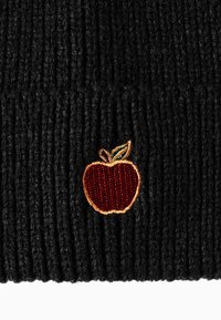 Beanie nero lavorato a maglia con texture a coste. Dettaglio notevole include una toppa ricamata a forma di mela rossa con accenti di foglie verdi.