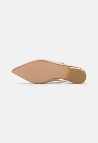 Zapato de tacón desnudo con punta afilada, material superior liso, suela beige y fondo texturizado con líneas de agarre y detalles de marca.
