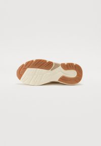 Suela de zapato con un diseño segmentado. Presenta una mezcla de goma beige, blanca y marrón, destacada con patrones de relieve para mayor agarre.