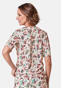 Bloemmotief top met korte mouwen van zacht roze stof. Opvallende groene en rode bloemontwerpen, gladde textuur, relaxte pasvorm.