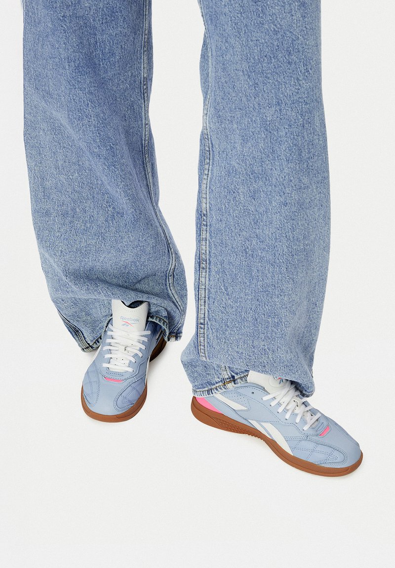 Asmuo, vilkintis šviesiai mėlynus "Reebok" sportbačius su baltais raišteliais ir guminiu padu, derinamas su laisvai krentančiomis šviesiai mėlynomis džinsinėmis kelnėmis.