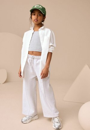 Weißes Hemd über einem grauen Crop-Top, kombiniert mit hellgrauen, weiten Sweatpants und silbernen Sneakers. Grüner Hut mit Textdetail.