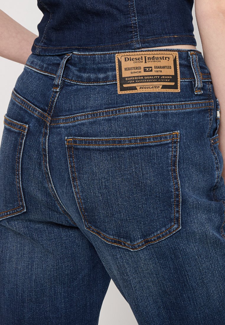 Jeans in denim blu scuro con un'etichetta in pelle marrone sul retro, dotati di tasche posteriori standard e dettagli di cucitura visibili.