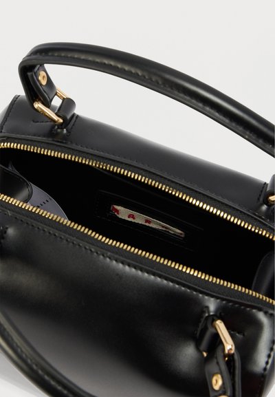 Μαύρη δερμάτινη τσάντα χειρός με φερμουάρ στην κορυφή, χρυσά μεταλλικά στοιχεία και λεία υφή. Το εσωτερικό διαθέτει ετικέτα και άφθονο χώρο αποθήκευσης.