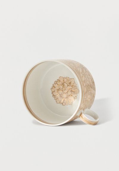 White ceramic cup with beige and gold floral patterns inside and outside, lying on its side with handle visible on a white background.