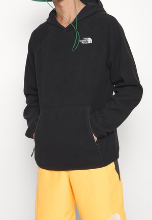 Musta fleece-huppari, jossa kiristysnauhallinen huppu, vetoketjullinen etutasku ja North Face -logo rinnassa.