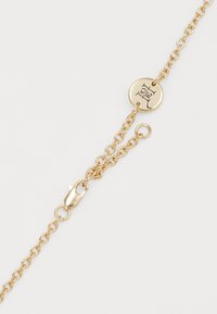 Guldarmband med cirkulär lås som har ett ingraverat logotyp. Länkarna är små och runda, vilket ger ett delikat utseende.