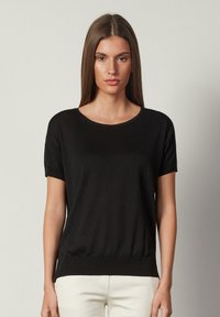 Svart kortärmad topp med rund halsringning och åtsittande fåll. Tillverkad av ett slätt, lätt tyg. Avslappnad och minimalistisk design.