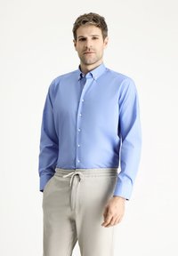 Camisa de botón de manga larga de color azul claro con cuello puntiagudo, hecha de una tela suave, combinada con pantalones de chándal beige con cordón.