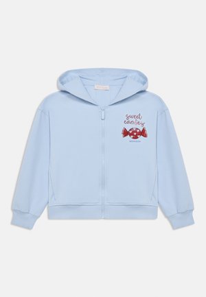 Svetlo modra jopa z zadrgo iz mehke tkanine. Ima kapuco, rebraste manšete in roza/rdeč sladkarijski grafični motiv z besedilom "sweet candy".