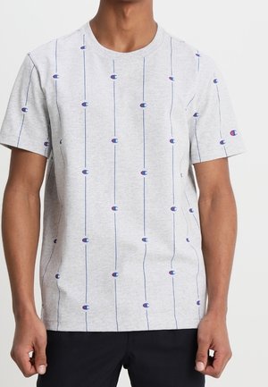 Man draagt een lichtgrijs T-shirt met korte mouwen, voorzien van verticale blauwe lijnen en kleine blauwe en rode "C"-logo's verspreid over het shirt.