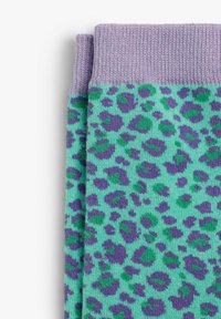 Calcetines turquesa con un estampado de leopardo púrpura. Puño de lavanda con canalé, textura de punto suave, con tonos de manchas verdes y moradas.