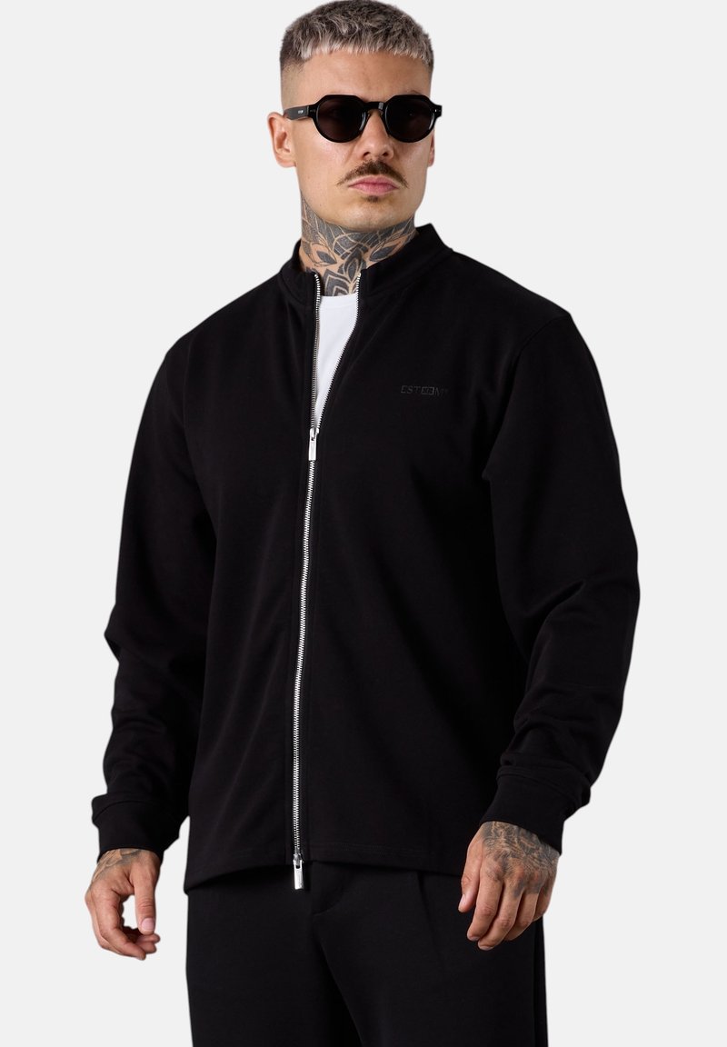 Schwarze Zip-Jacke aus weichem Stoff mit hohem Kragen, unsichtbaren Nähten, langen Ärmeln und slim fit Schnitt.