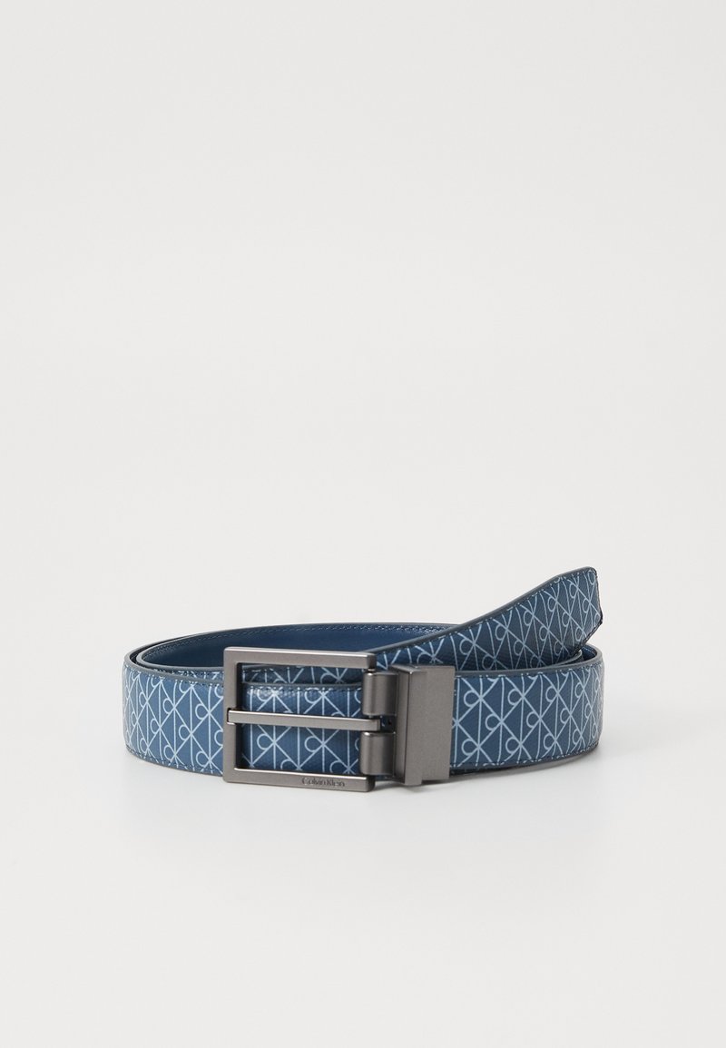 Ceinture en cuir bleu avec un motif géométrique répétitif bleu clair et une boucle rectangulaire en argent mat, enroulée sur un fond blanc.
