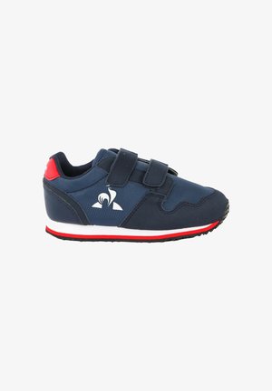 Marineblauwe sneaker met twee klittenbandriempjes, witte en rode zool, rood hielaccent en wit gestileerd vogel-logo aan de zijkant.