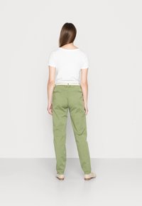 Gröna bomullsbukser med avslappnad passform, med två bakfickor, ett lätt midjeband och en mjuk textur. Matcher med en vit t-shirt.