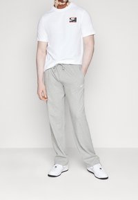 Vit t-shirt med kort ärm och en röd och svart Nike-logotyp, ihopparad med ljusgrå sweatpants som har en liten vit Nike-logotyp.