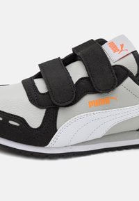 Zapatilla Puma en gris y negro con raya blanca, logo de Puma en naranja y dos tiras de velcro negras sobre un fondo blanco.