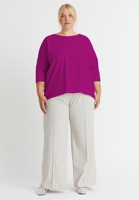Magenta Übergröße Oberteil mit 3/4 Ärmeln, kombiniert mit hellbeigen, hochgeschnittenen, weit geschnittenen Hosen und metallic-silbernen Schuhen. Einfaches Design.