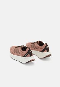 Baskets de sport rose clair avec tige en mesh, accents noirs et semelle en caoutchouc blanche. Présente des motifs texturés et un détail de logo sur le talon.