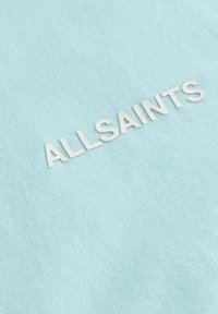 Šviesiai mėlynas medvilninis marškinėliai su pakeltu baltu tekstu "ALLSAINTS." Lygus audinys su minimalistiniu dizainu ir minkšta medžiaga.