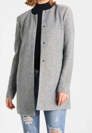 Cappotto di lana grigio con scollatura tonda, chiusura frontale con bottoni e maniche lunghe, abbinato a jeans blu strappati. Tessuto testurizzato.