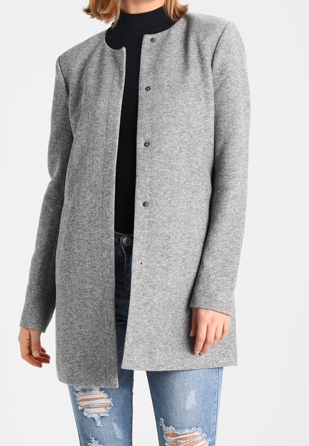 Cappotto di lana grigio con scollatura tonda, chiusura frontale con bottoni e maniche lunghe, abbinato a jeans blu strappati. Tessuto testurizzato.