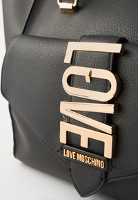 Fekete, texturált bőrtáska aranyszínű „LOVE” logóval és „LOVE MOSCHINO” felirattal a fedélen. Jellemző geometriai dizájn kiegészítők.