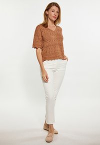 Top corto lavorato a maglia bronzeo con scollatura a V e maniche corte, abbinato a pantaloni bianchi attillati e scarpe beige senza lacci. Motivo semplice e testurizzato.