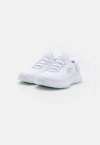 White athletic shoes with a mesh upper, textured finish, and elastic laces. Features a curved sole and subtle branding on the side.