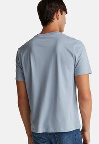 Světle modré bavlněné tričko s krátkým rukávem, kulatým výstřihem a volným střihem. Hladká textura, žádné viditelné vzory ani akcenty.