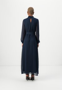 Μάυρο μακρύ φόρεμα με μακριά μανίκια και ρουφηχτό ντεκολτέ, με άνοιγμα στην πλάτη και ζώνη στη μέση; διαφανές ύφασμα με ρευστή σιλουέτα και μήκος που φτάνει μέχρι το πάτωμα.