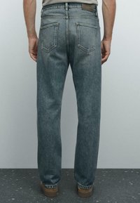 Denim jeans in a faded blue-gray color, featuring a straight leg, five-pocket design, and visible stitching details on the back.