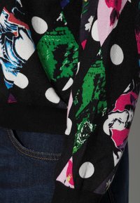 Strikket sweater med en sort bund, prydet med farverige blomster- og prikmønstre. Ærmerne er ribbede; stofstrukturen er blød.