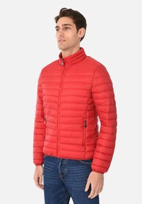 Giacca puffer rossa con colletto alto, chiusura a zip e tasche laterali. Presenta sezioni trapuntate orizzontali e una texture liscia.
