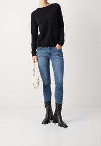 Czarny sweter z długim rękawem, niebieskie obcisłe jeansy i czarne botki z kwadratowymi noskami. Jasna torebka trzymana w prawej ręce.